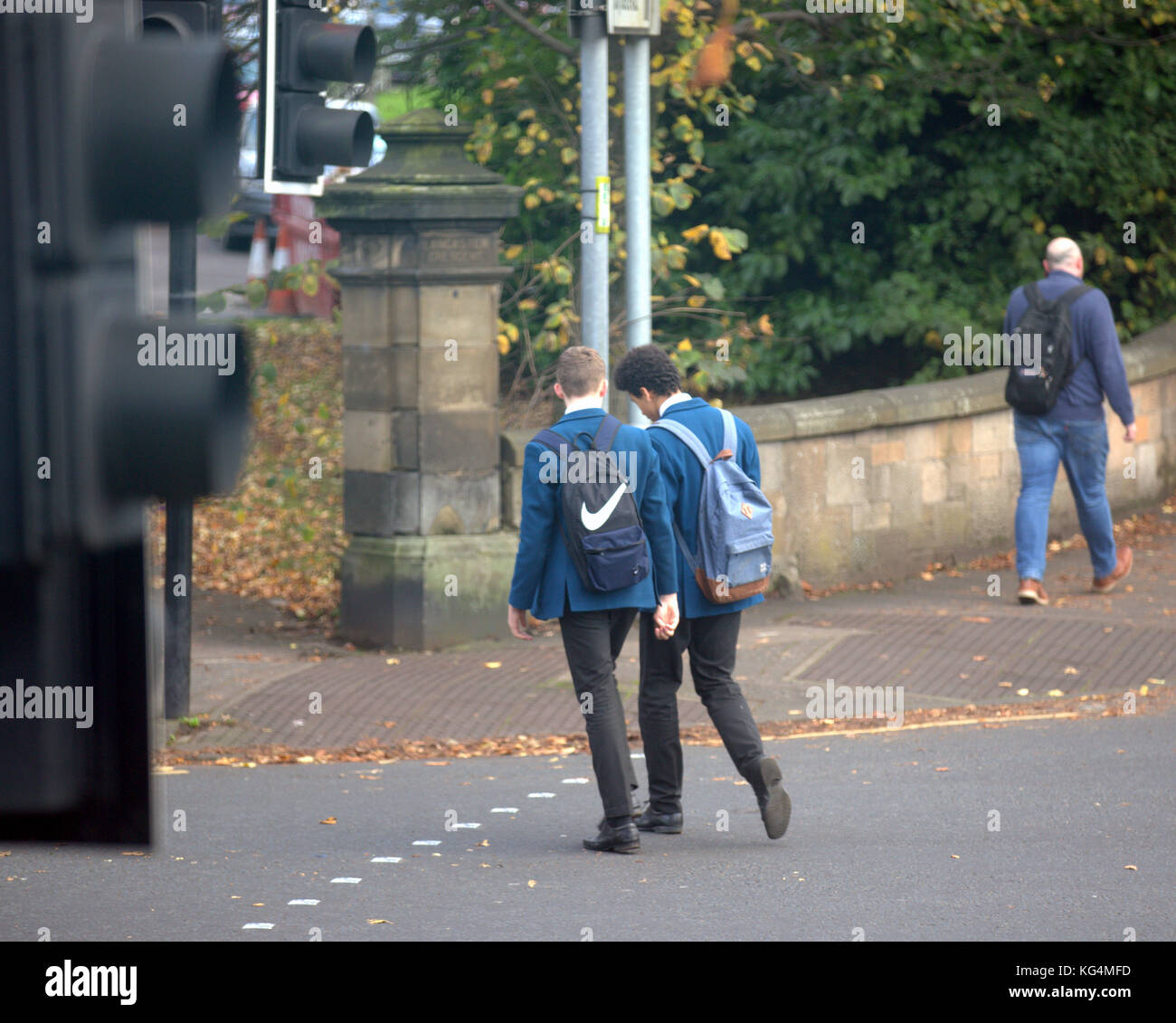 Britische Schüler Jungs in Uniform Schule überqueren Sie die Straße an der Ampel in der Straße aus gesehen hinter Stockfoto
