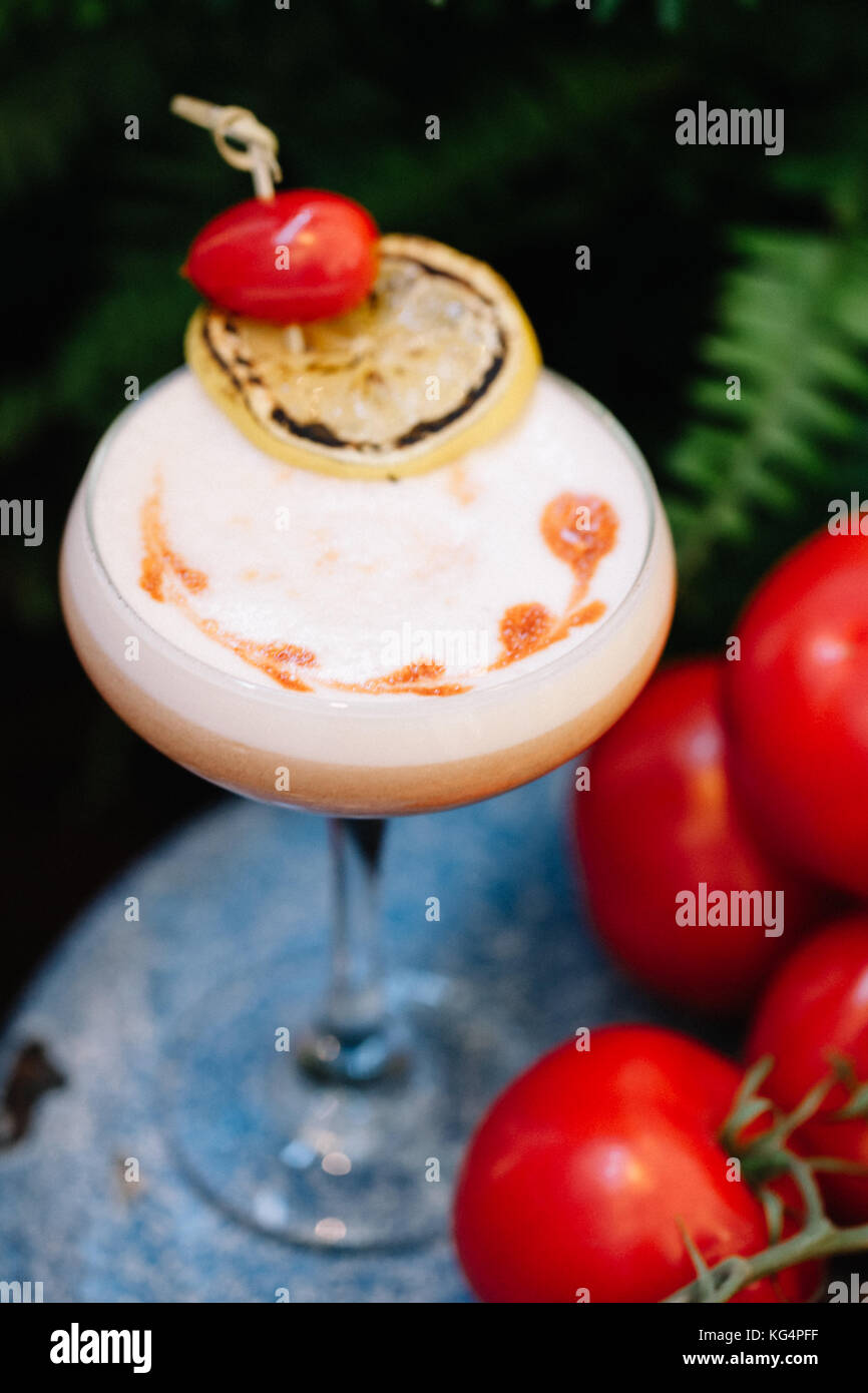 Einen alkoholfreien Cocktail mit Schaum, garniert mit Trauben Tomaten und eine Scheibe geräucherter Zitrone neben einem Cluster von reifen Tomaten Stockfoto
