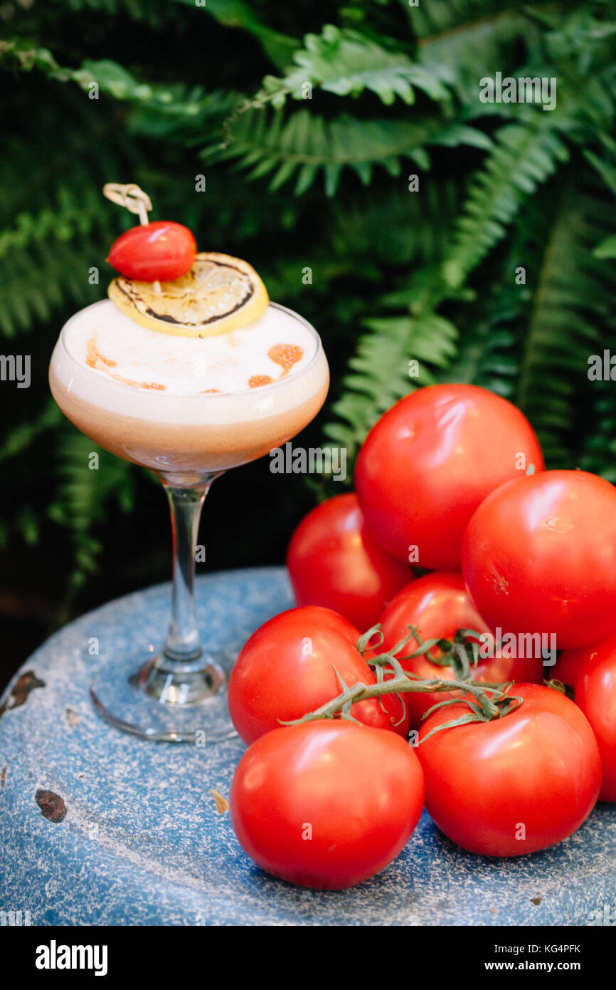 Einen alkoholfreien Cocktail mit Schaum, garniert mit Trauben Tomaten und eine Scheibe geräucherter Zitrone neben einem Cluster von reifen Tomaten Stockfoto