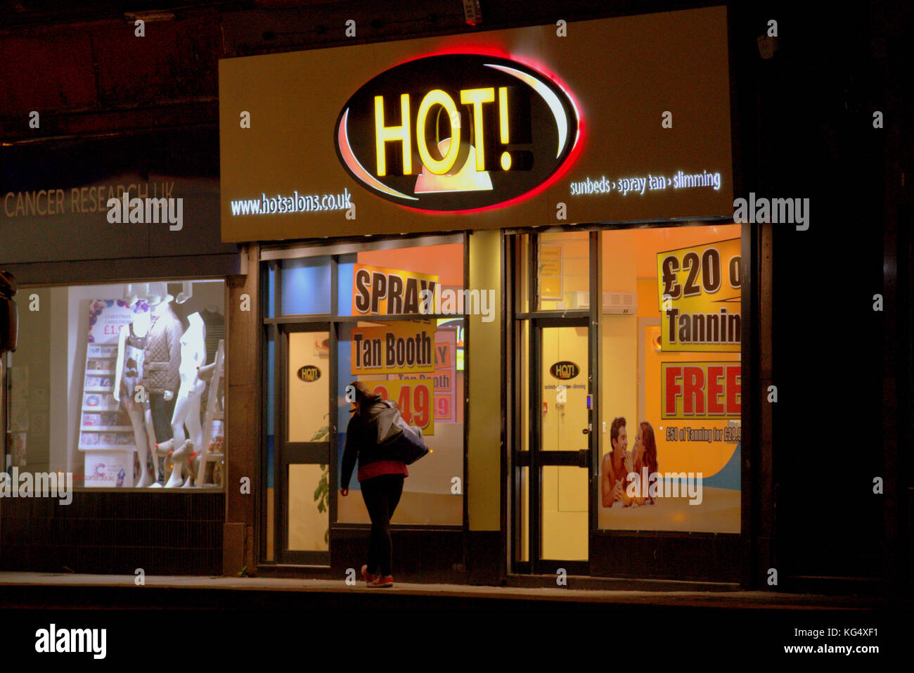 Hautkrebs Sorge uv-hot Sonnenbank Shop neben der Krebsforschung Charity Shop Kunde aus gesehen hinter bei Nacht Stockfoto