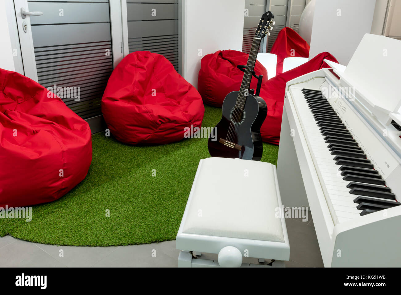 Moderne Musik - Zimmer, mit weißen Klavier und Gitarre Schwarz; Rot  Sitzsäcke im Hintergrund Stockfotografie - Alamy