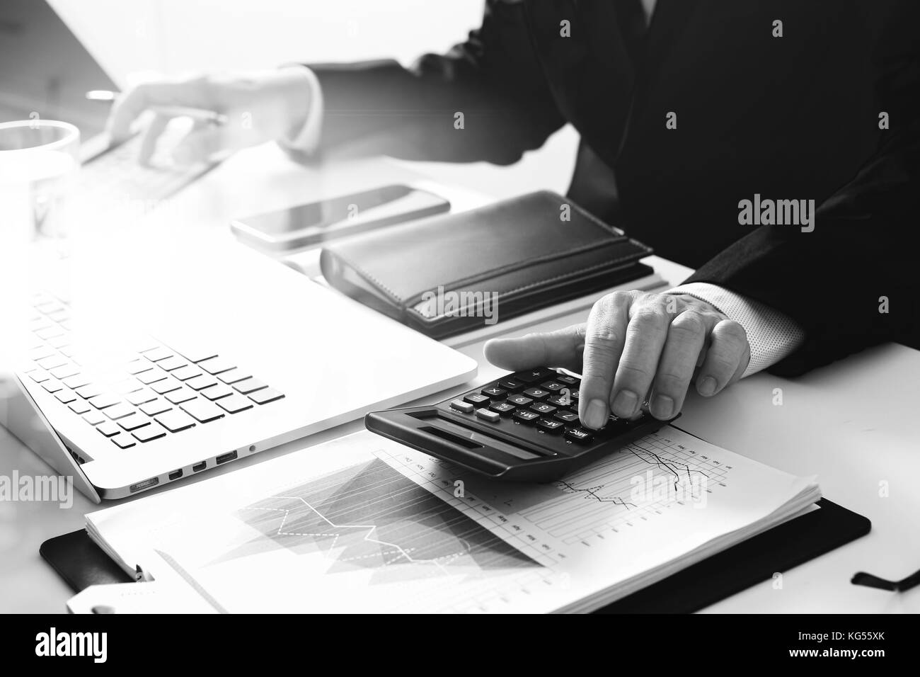 Geschäftsmann wird das Arbeiten mit Finanzen zu Kosten und Rechner und Laptop mit Handy auf mit Schreibtisch in modernen Büro, Schwarz und Weiß Stockfoto