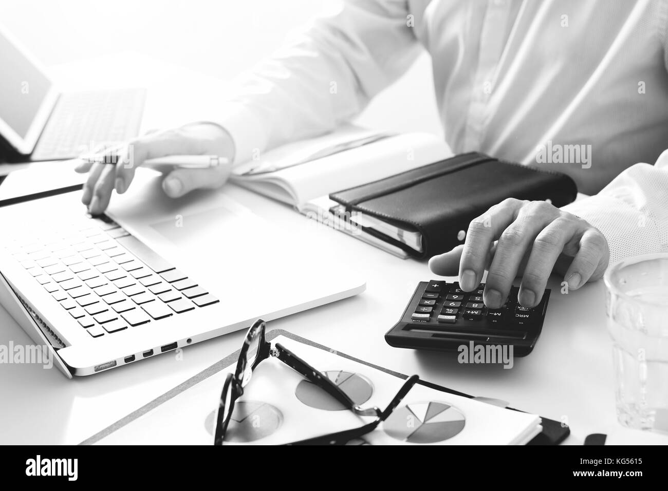 Geschäftsmann wird das Arbeiten mit Finanzen zu Kosten und Rechner und Laptop mit Handy auf mit Schreibtisch in modernen Büro, Schwarz und Weiß Stockfoto