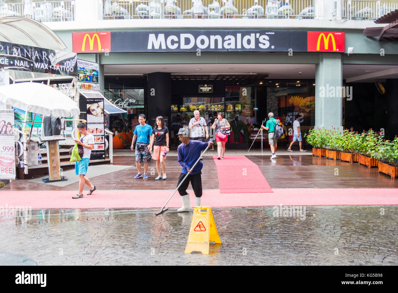 Ein Arbeiter fegt überschüssiges Wasser außerhalb der Eingang zu McDonalds, Jung Ceylon Einkaufszentrum, Patong, Phuket, Thailand Stockfoto