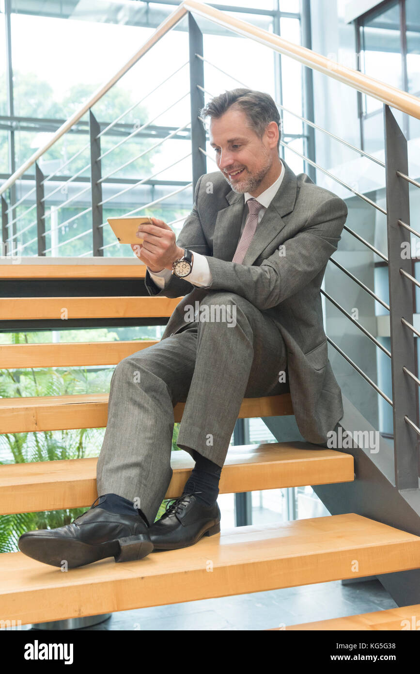 Mann in Business Kleidung sitzt mit Smartphone auf Treppen Stockfoto