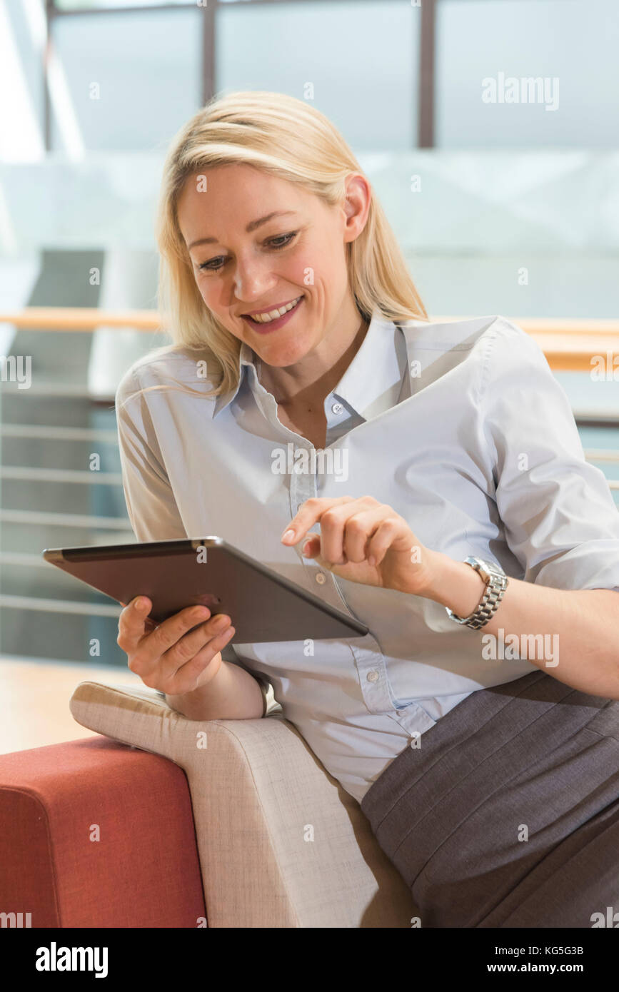 Blonde Frau schaut lächelnd auf Ihrem Tablet-PC Stockfoto