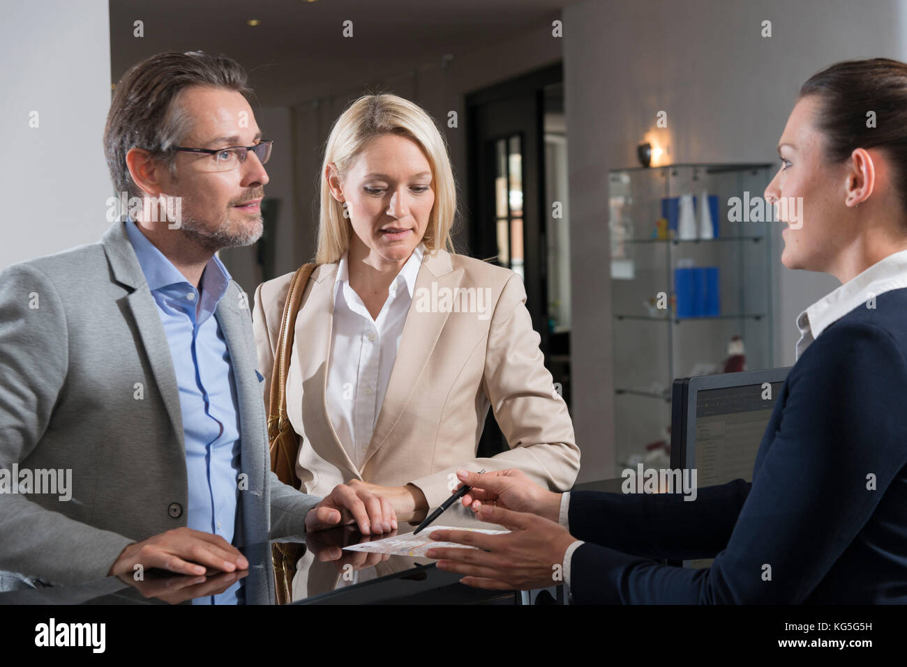 Mann und Frau im Gespräch mit dem Rezeptionisten im Hotel Stockfoto