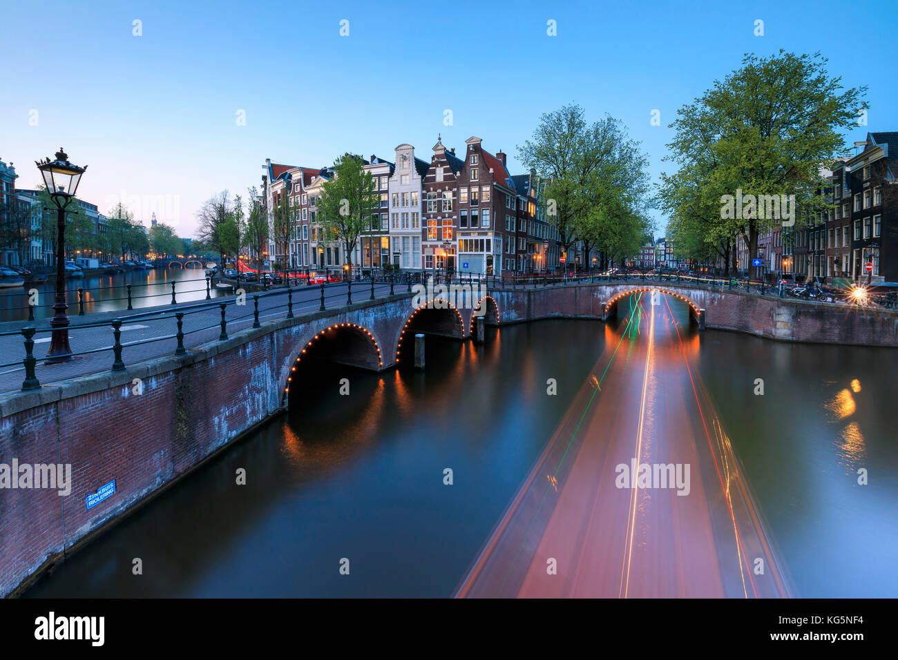 Dämmerung leuchtet auf die typischen Gebäude und Brücken spiegeln sich in einer typischen Kanal Amsterdam Holland die Niederlande Europa Stockfoto