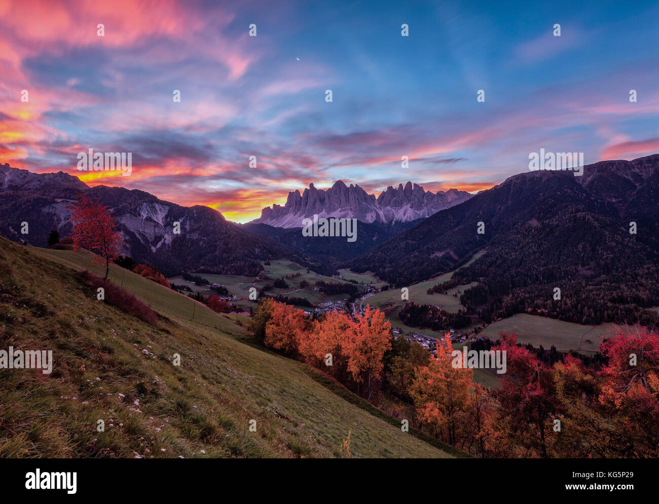 Bunte Herbstbäume umrahmen die Geislergruppe und das Dorf St. Magdalena bei Sonnenaufgang im Funes Tal Südtirol Dolomiten Italien Europa Stockfoto