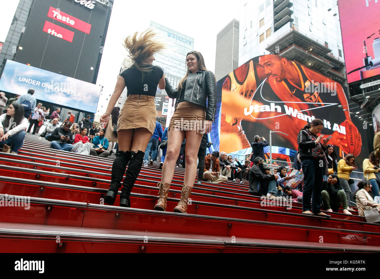 Zwei junge weibliche Touristen Spaß posieren für Fotos an den Treppen im Herzen des Times Square. Stockfoto