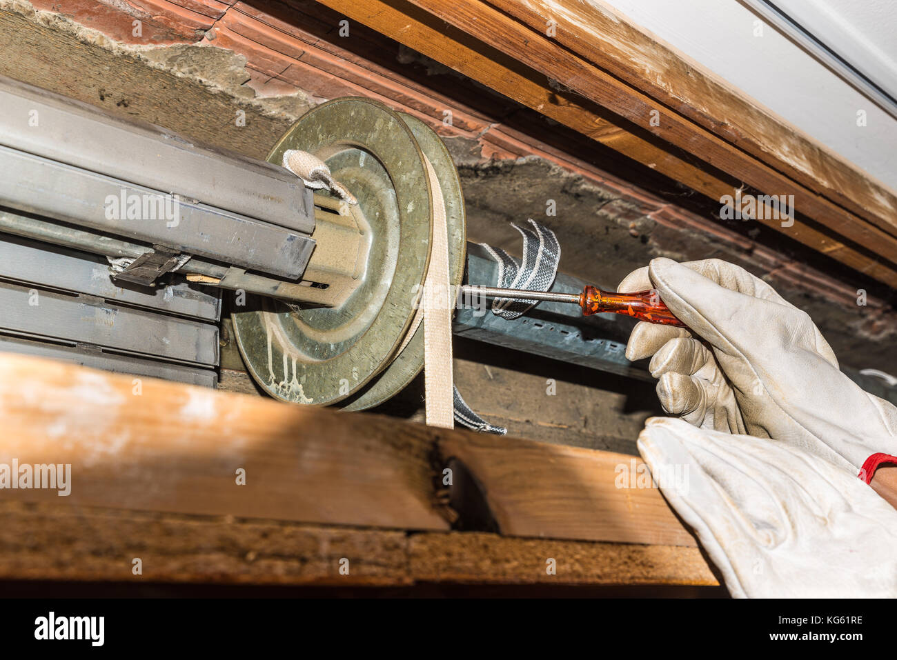 Rolling Shutter reparieren. Arbeitnehmer stellt einen defekten Rollladen von zu Hause. Nahaufnahmen der Hände mit Handschuhen und orange Starter Schraubendreher Stockfoto