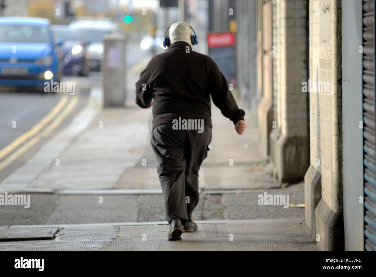 Fat man Junge mit Kopfhörer zu Fuß auf der Straße aus gesehen hinter Stockfoto