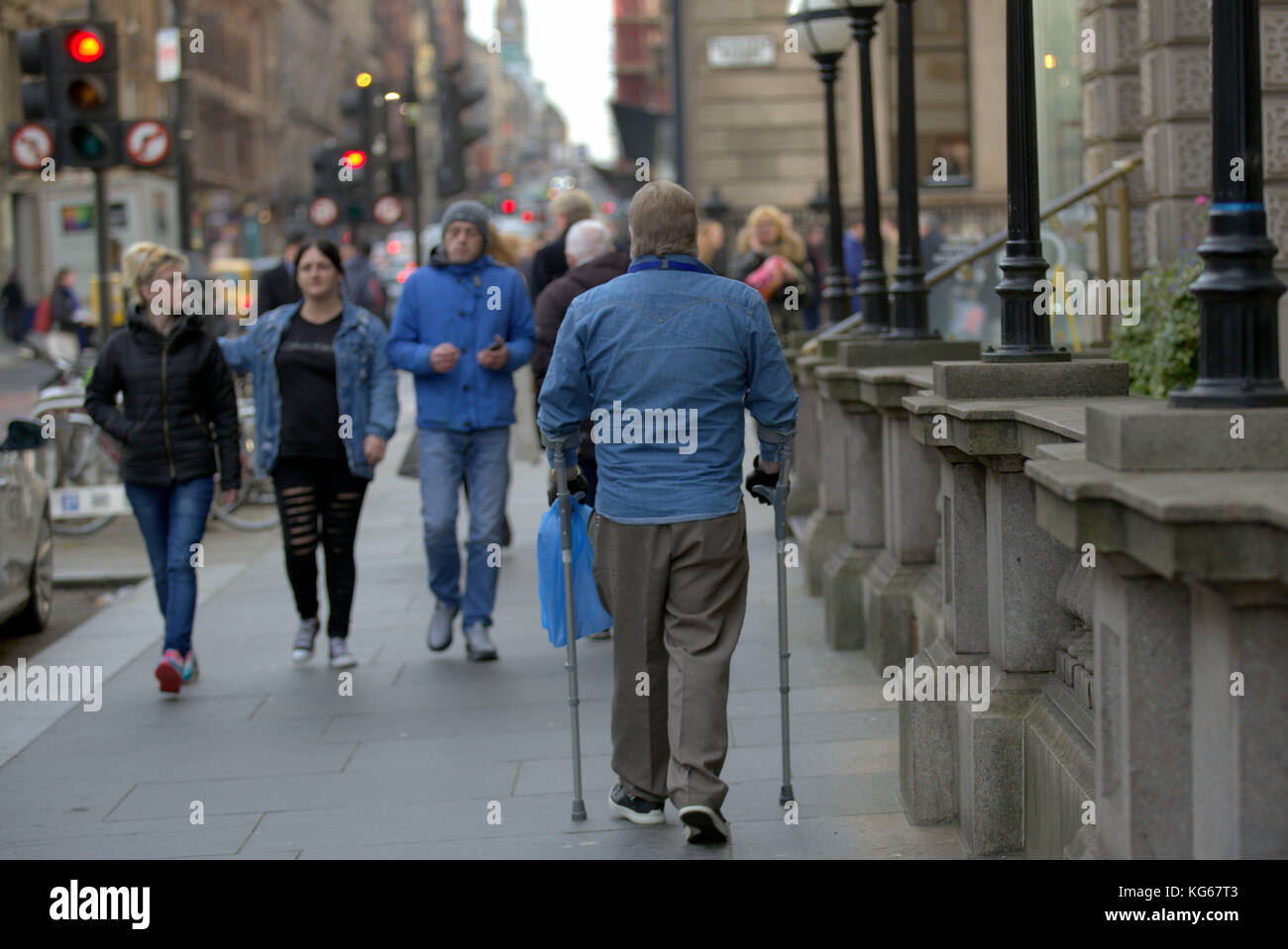 Mann auf Krücken zu Fuß auf der Straße aus gesehen hinter der Stadt Glasgow, Vereinigtes Königreich Stockfoto