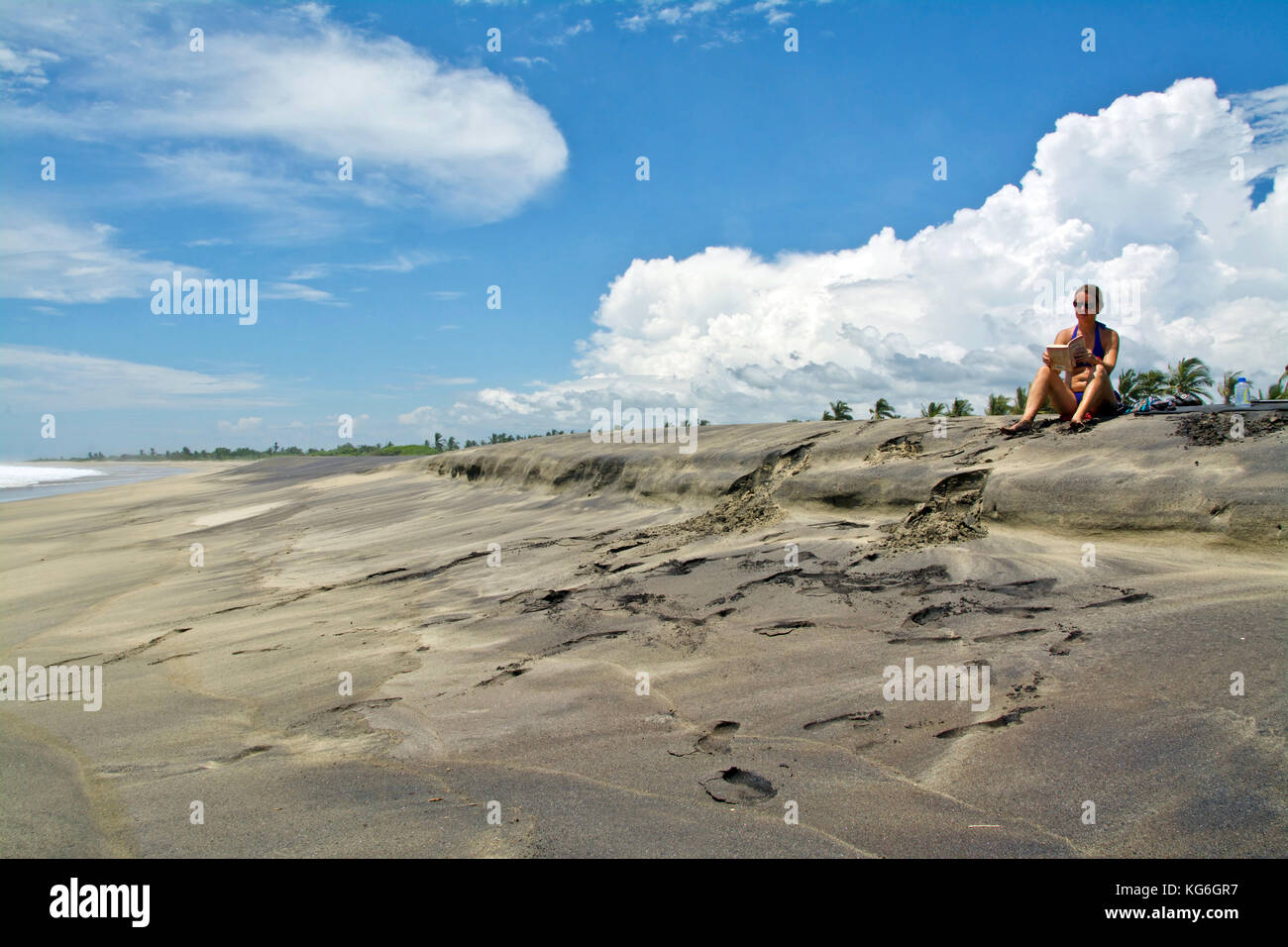 Kaukasische Frau liest ein Buch in dem schönen Strand unter blauem Himmel Stockfoto