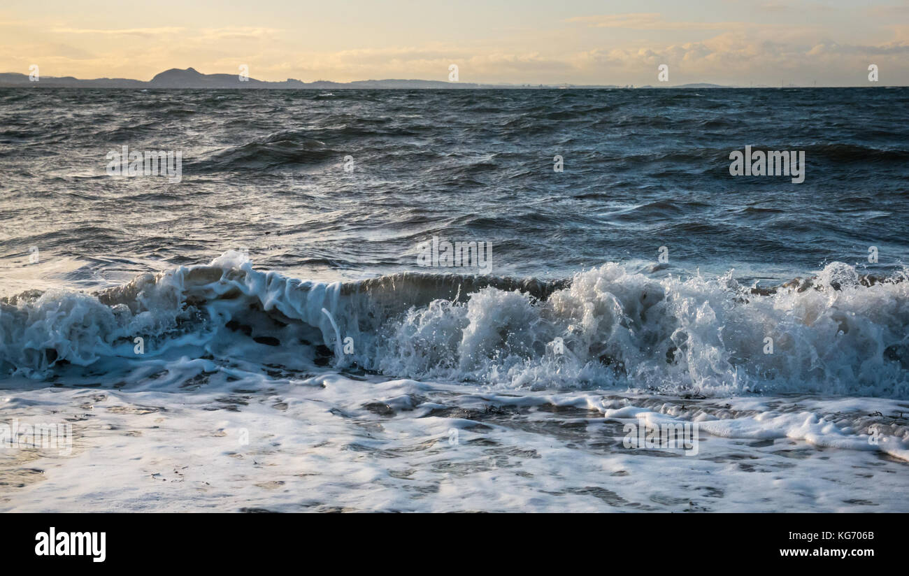 Kleine schaumige Wellen am Strand in die Firth-of-Forth brechen in Richtung der charakteristischen Umrisse von Arthur's Seat in der Ferne, Schottland, Großbritannien Stockfoto