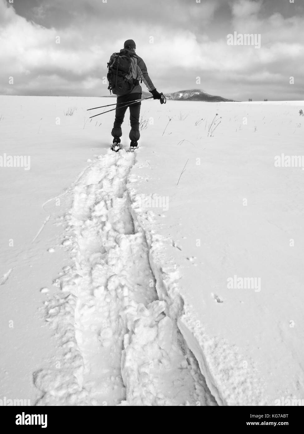 Wanderer mit Rucksack Schneeschuhwandern im tiefen Drift. Mann mit Schneeschuhen gehen im Hill. Wanderer in Grün Grau winter Jacke und schwarzen trekking Hose snowsho Stockfoto