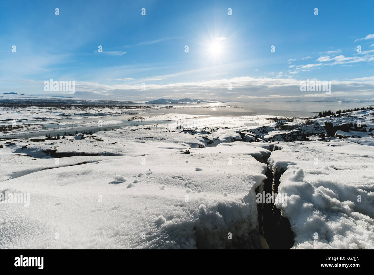 Winterlandschaft, Risse im Schnee bedeckten Boden mit der Sonne am blauen Himmel, in pingvellir Nationalpark in Island Stockfoto