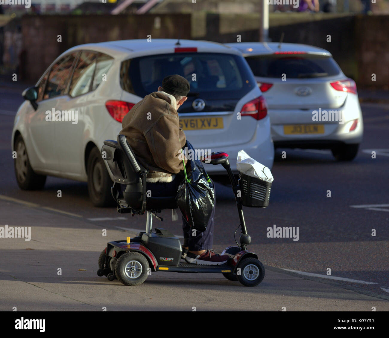 Alter Mann auf der elektrischen Mobilität scooter Warten besetzt Strasse aus gesehen hinter Stockfoto