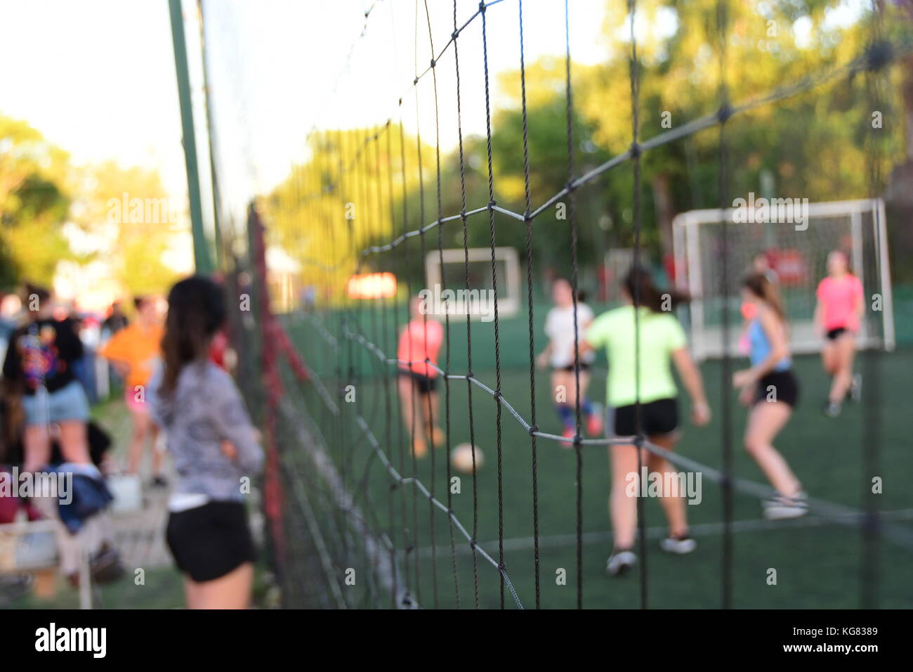 Verschwommene Teenage Mädchen spielen Fußball im Freien, wie durch ein Netz an einem sonnigen Frühlingsnachmittag in den Vororten gesehen Stockfoto