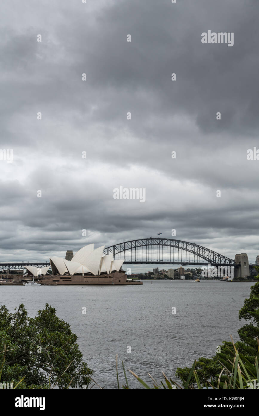Sydney, Australien - 23. März 2017: Portrait von weißen Oper und schwarzen Schleife der Harbour Bridge hinter unter schwerem Regen cloudscape. grau Hafen wat Stockfoto