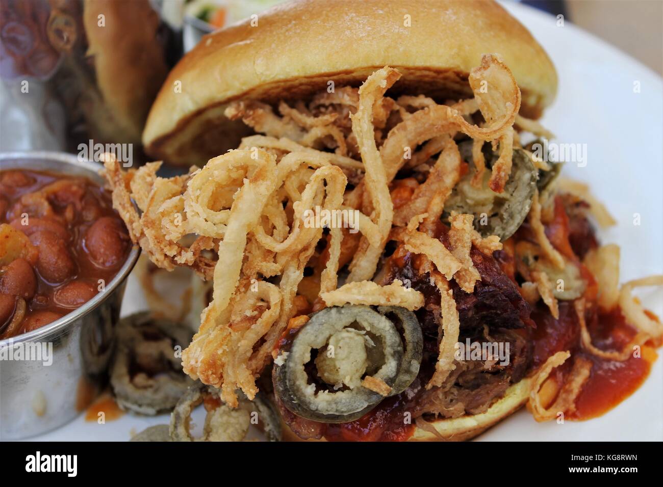 Zog pork Sandwich mit frittierten Zwiebeln und Jalapenopfeffer, und eine Seite von Baked Beans, auf einem Bürgersteig Tabelle in Key West, Florida, USA. Stockfoto