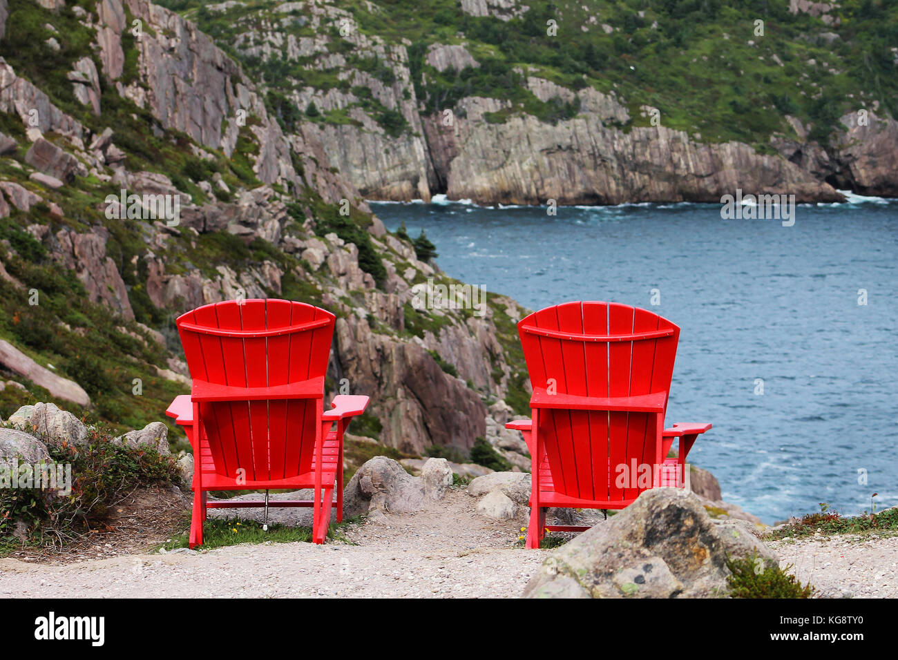 Blick von hinten zwei rote Adirondack Stühle auf der Klippe verankert, mit Blick auf die Bucht. Signal Hill Wanderwege, St. John's, Neufundland. Stockfoto