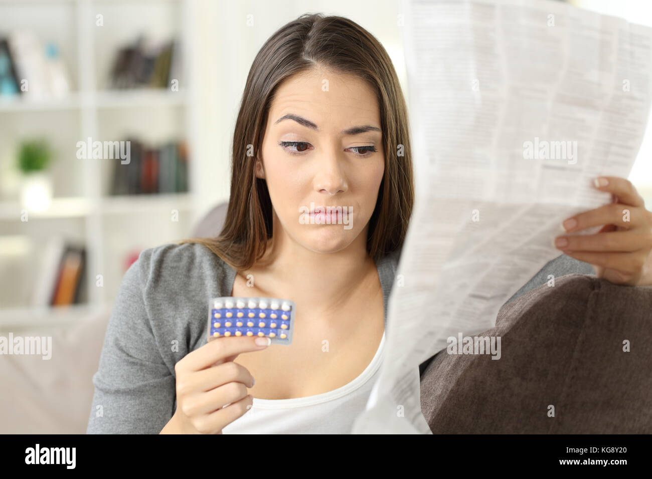 Verdächtige Frau liest eine Broschüre nach der Einnahme von empfängnisverhütenden Pillen sitzen auf einer Couch im Wohnzimmer in einem Haus innen Stockfoto
