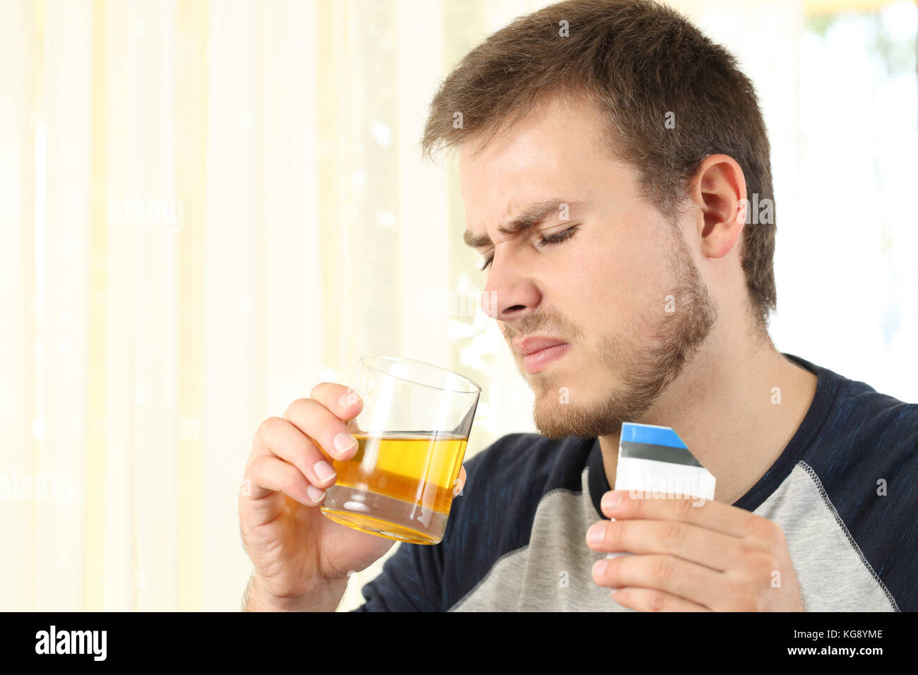 Angewidert Mann trinkt ein Medikament mit schlechtem Geschmack zu Hause Stockfoto