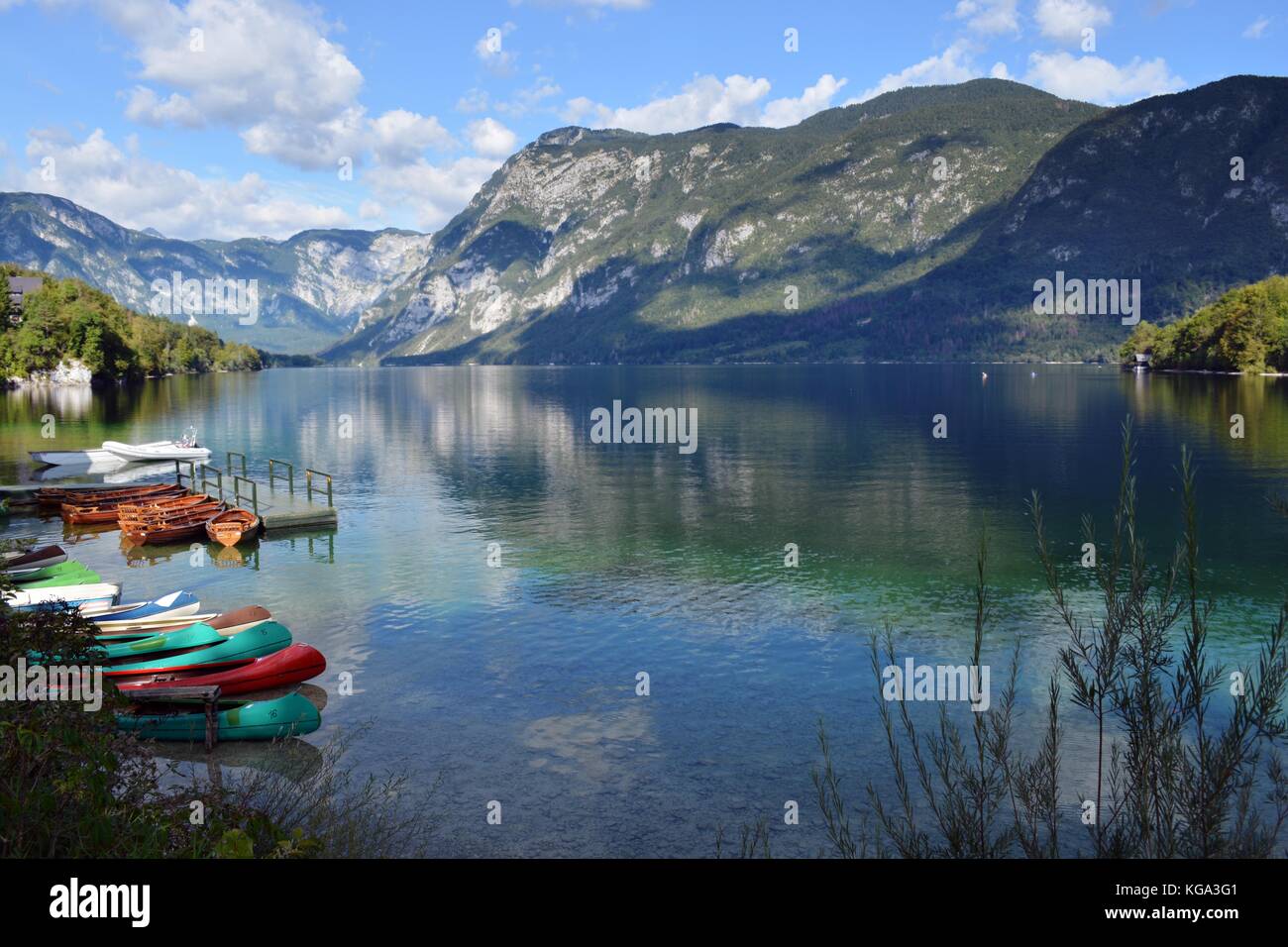 Boote am Ufer des Sees von Bohinj und der Himmel und die Berge im See spiegeln Stockfoto