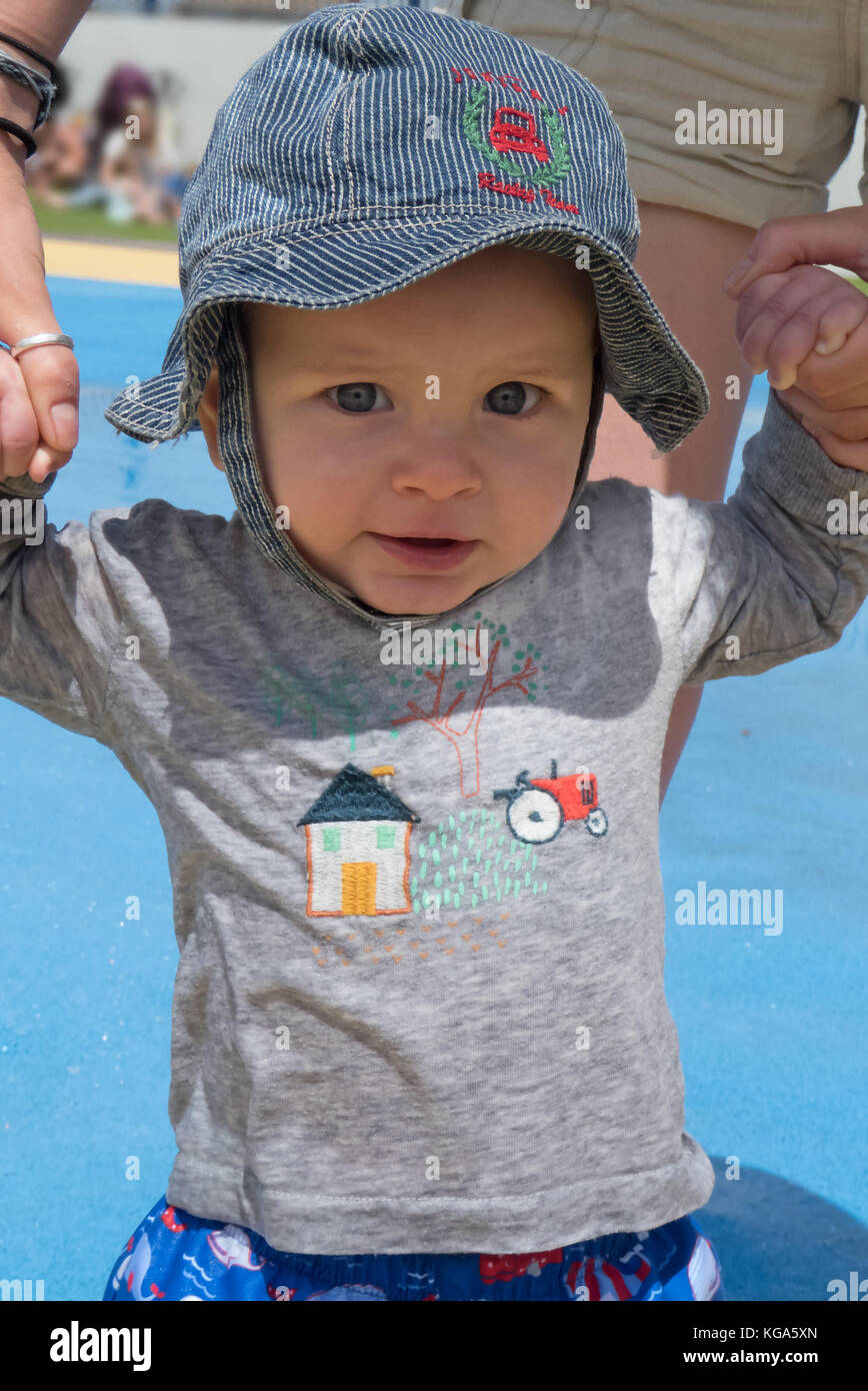 Acht Monate alten Baby boy in einer Diskette sun-hat, halten sich an den Händen und half zu gehen. MODEL RELEASED Stockfoto