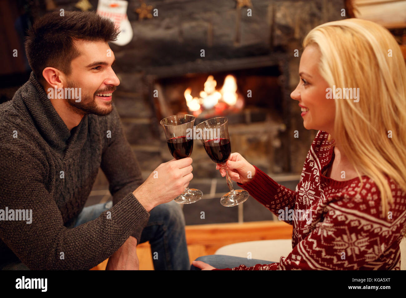Lächelnde Frau und Mann toasten lecker Rotwein am romantischen Kamin Stockfoto