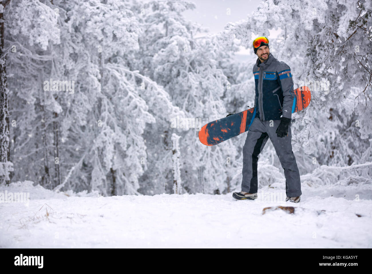 Lächelnder Mann mit seinem Snowboard Ski Maske, extreme Sport- und Winterurlaub Holding auf dem Berg Stockfoto