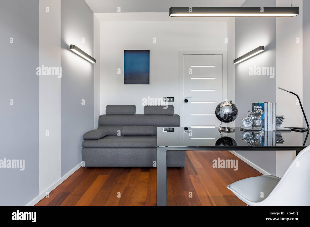 Home Office mit schwarzem Glastisch, weißem Stuhl und grauer Couch Stockfoto