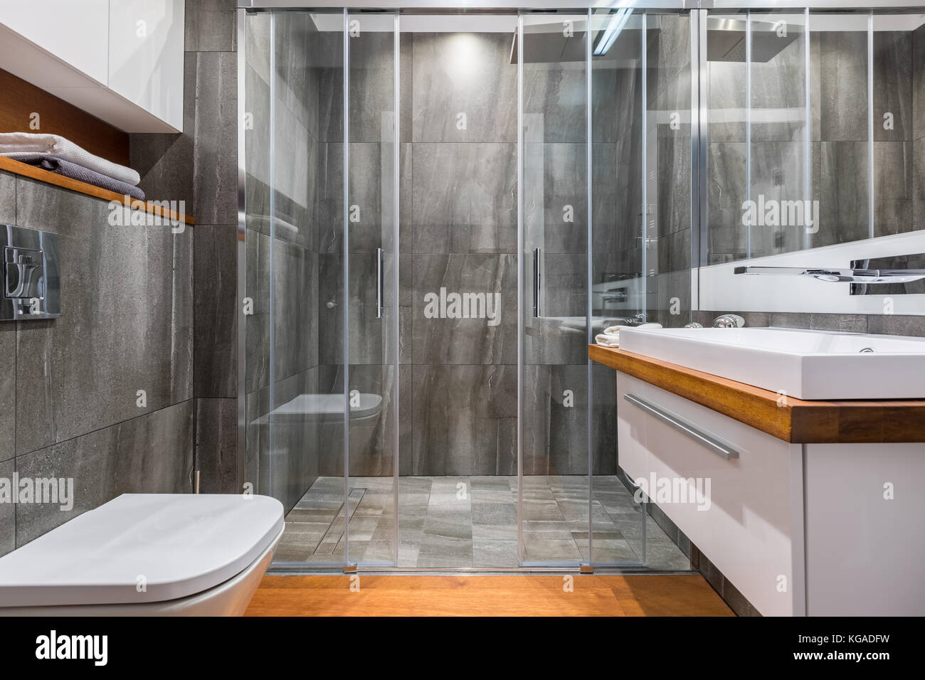 Graues Badezimmer mit weißem Waschbecken, Toilette und eleganter begehbarer Dusche Stockfoto