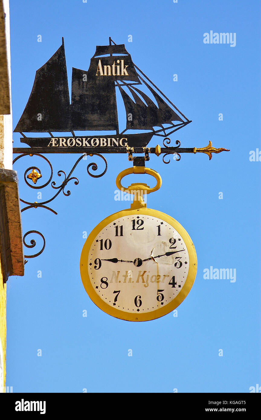 Aeroskobing, Dänemark - 4. Juli 2012 - Metallgeschäft Zeichen eines Antiquitätenladens in Form eines Segelschiffes mit Vintage Uhr darunter vor einem blu Stockfoto