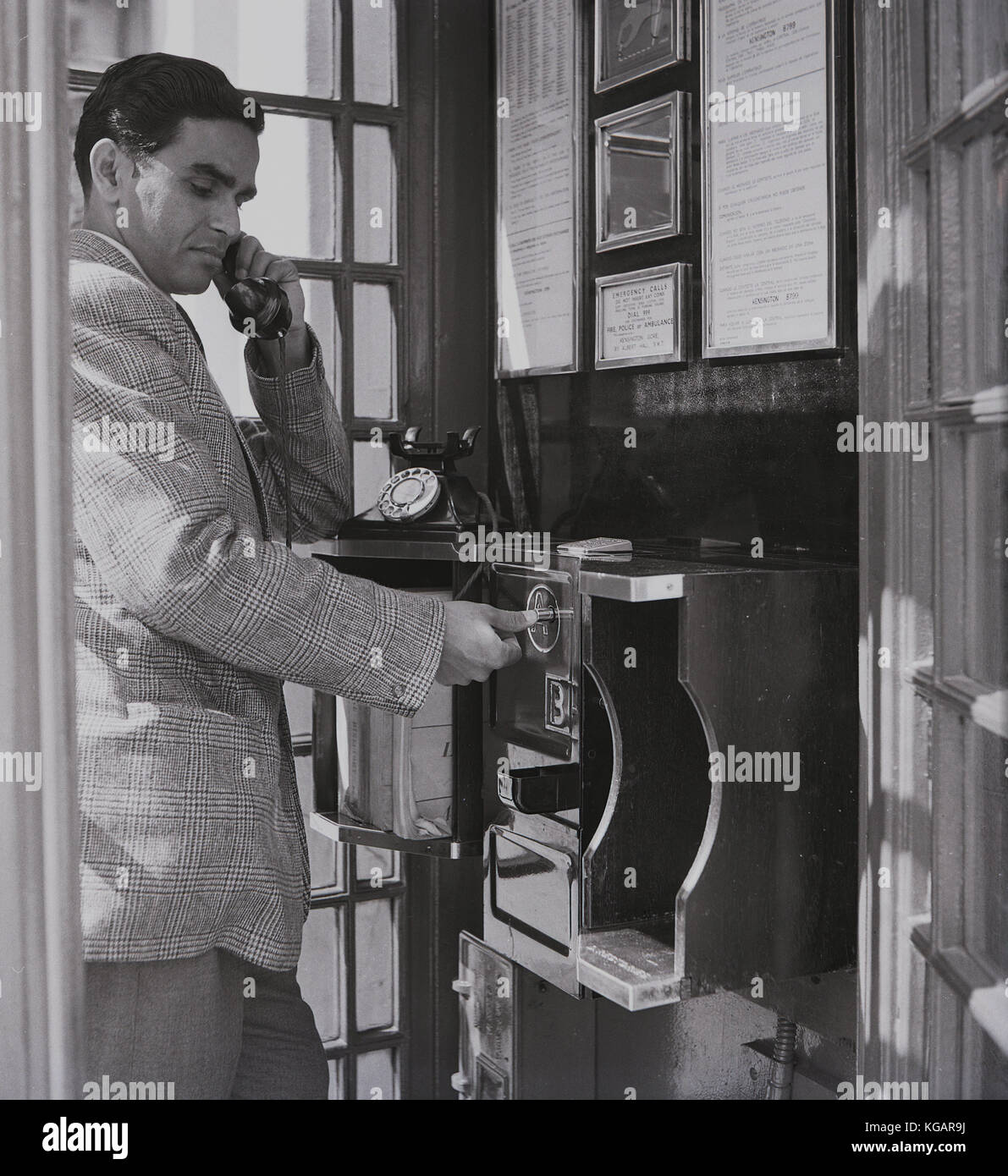 1950er Jahre, historisch, ein männlicher Übersee-Besucher in England, der einen Anruf von einer öffentlichen Telefonzelle in Kensington Gore, London, macht. Nachdem er seine Münzen eingelegt hat, drückt er kurz vor dem Anruf Taste A, wenn der Empfänger seinen Anruf entgegennimmt. Stockfoto