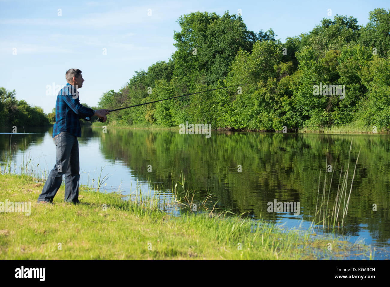 Hobby Angler mit der Rute steht am Ufer in der Nähe des ruhigen, kleinen und schmalen Flusses. Unscharfe grünen Wald im Hintergrund. Stockfoto