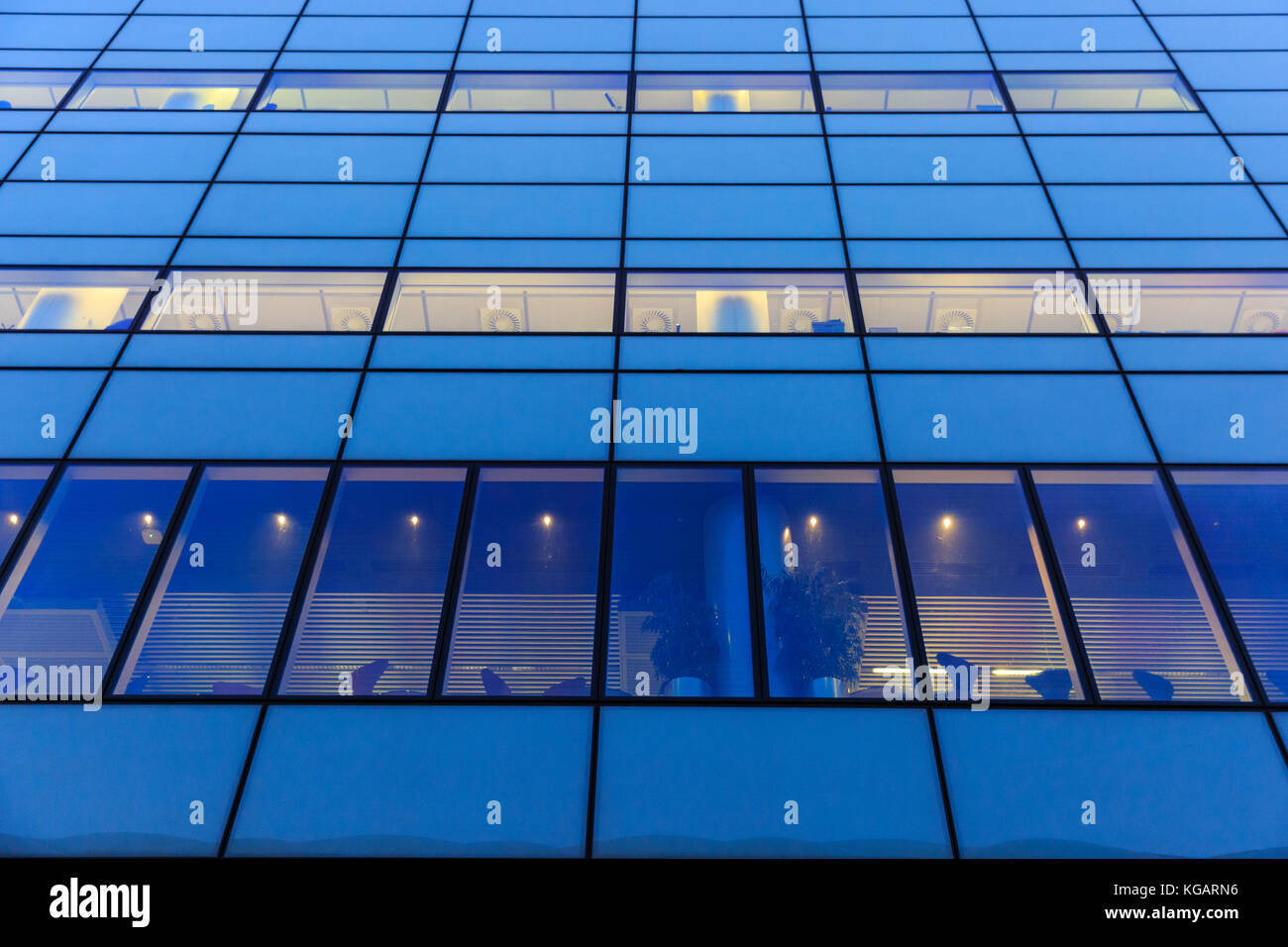 Blau gefärbte Bürofassade mit geometrisch gemusterten Fenstern und warmer Innenbeleuchtung, London, Großbritannien Stockfoto