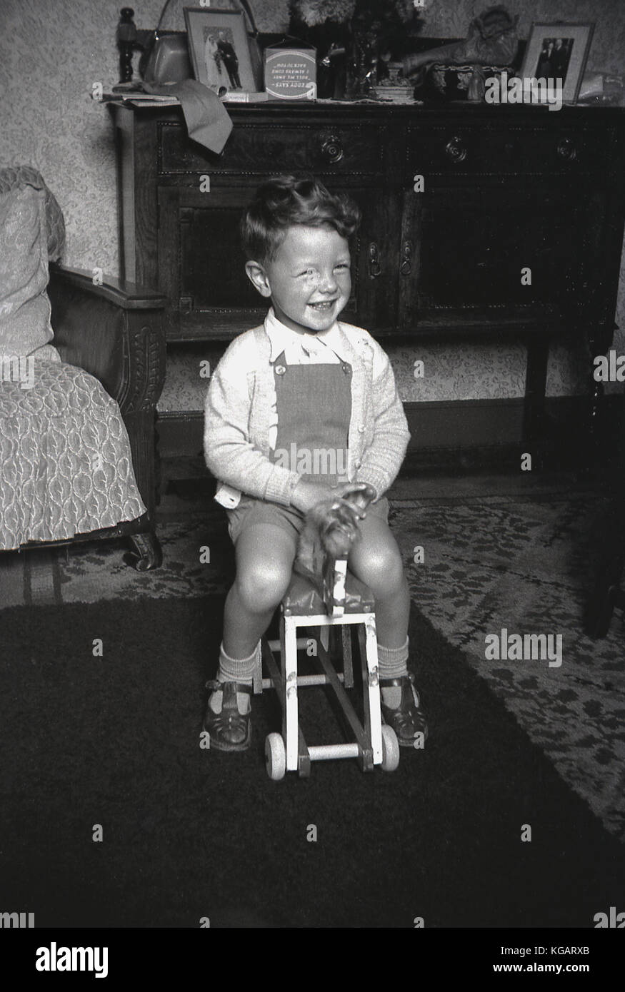 1940, Großbritannien, kleinen Jungen zu Hause im vorderen Zimmer saß auf seinem Holzspielzeug Pferd mit Rädern. Stockfoto