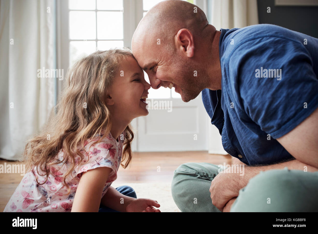 Vater und Tochter sitzen auf dem Boden zu Hause berühren Köpfe Stockfoto