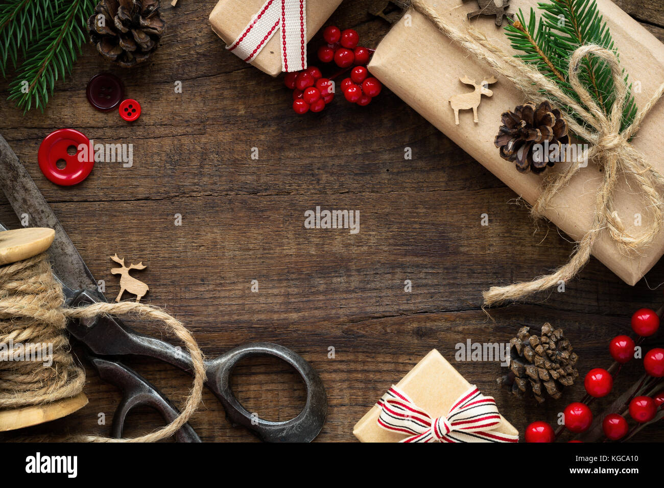 Weihnachten - Weihnachtsgeschenk in braunes Packpapier eingewickelt, sackleinen Garn, vintage Schere, rote Tasten, Rentiere, Tannenzweigen und Tannenzapfen. Flach, über Stockfoto
