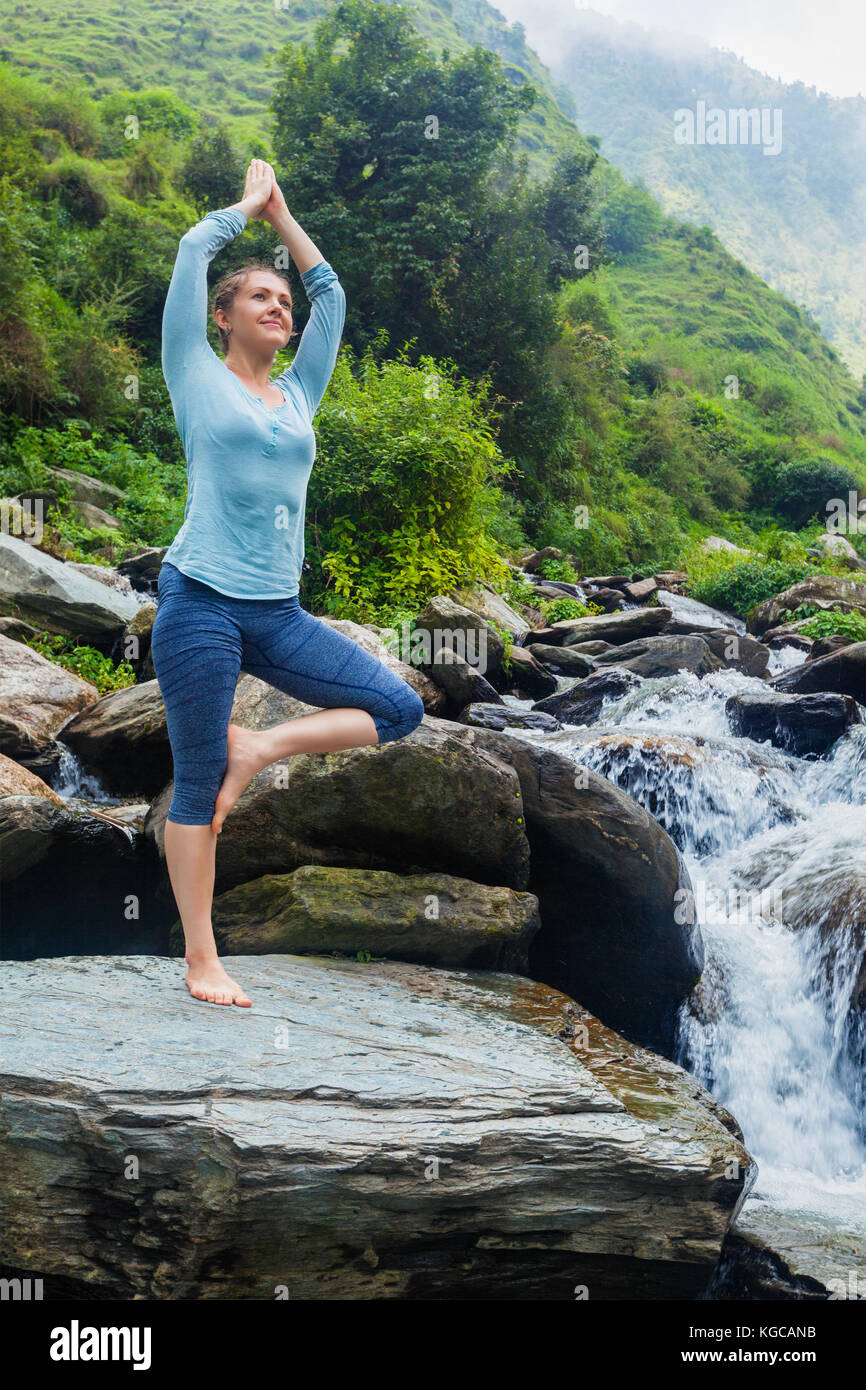 Frau in Yoga Asana Vrikshasana Baum am Wasserfall im Freien Stockfoto