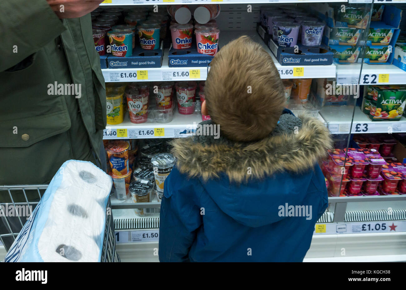Ein 6-jähriger Junge in einer warmen Winterjacke, der Joghurt im Tesco Supermarkt, Schottland, Großbritannien, auswählt Stockfoto