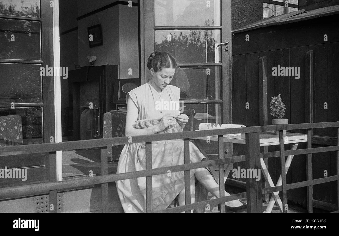 1940, Großbritannien, junge Frau ein Kleid allein sitzen auf einem Haus Veranda stricken. Hand - stricken war ein beliebter Zeitvertreib für Frauen während dieses Krieges. Stockfoto