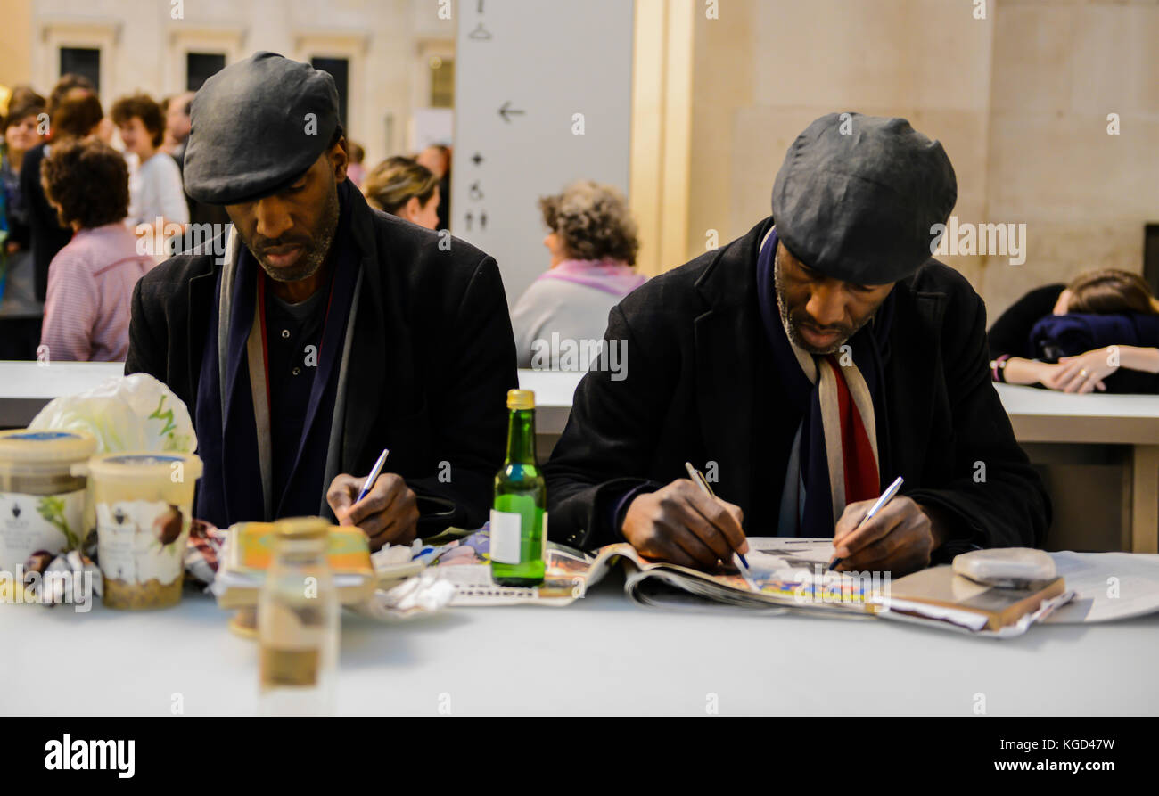 Zwei eineiige Zwillinge schreiben Sie mit beiden Händen auf einer Zeitung in ein Café. Stockfoto