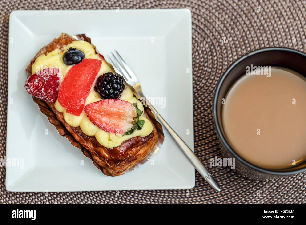 Ein Becher Kaffee und Obst Gebäck auf eine weiße Platte mit einer kleinen Gabel Stockfoto