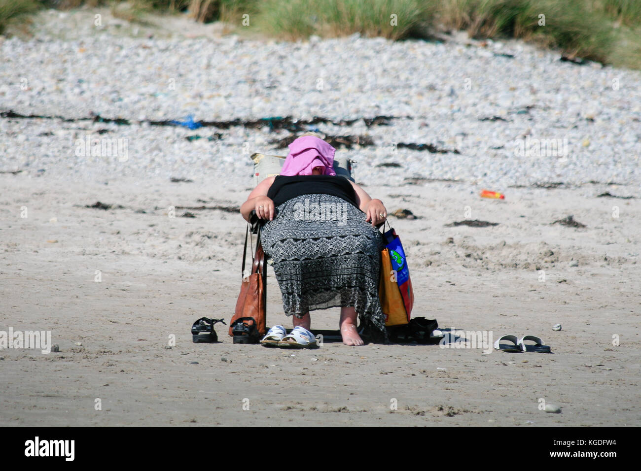 Frau, die auf einem Stuhl liegt, bedeckt ihr Gesicht, um sich vor der starken Mittagssonne an einem Keel-Strand in Keel, Achill Island, County Mayo, Irland, zu schützen Stockfoto
