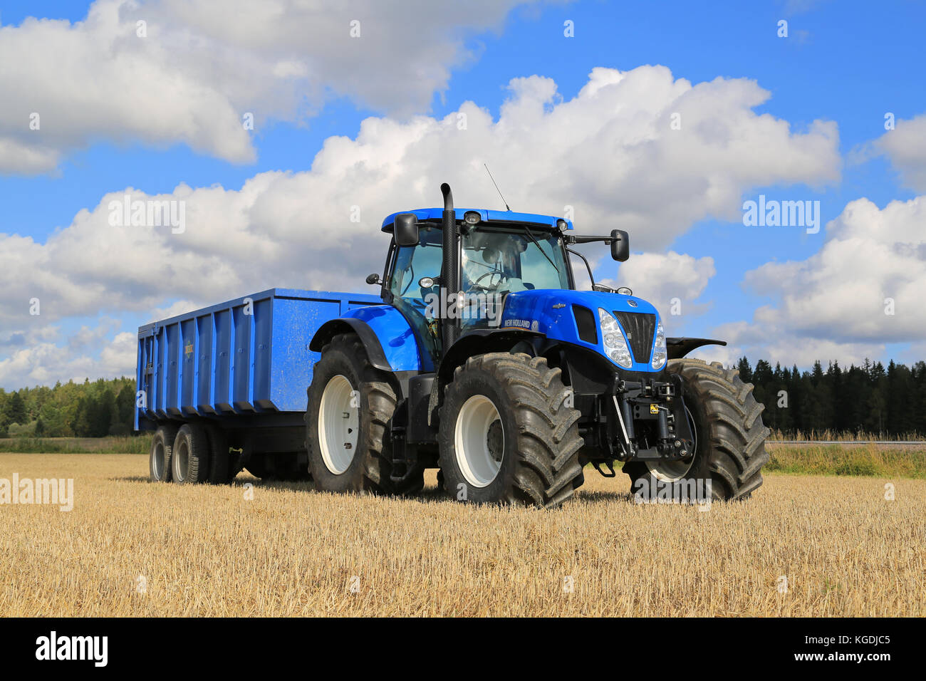 Somero, FINNLAND - 12. SEPTEMBER 2015: New Holland T 7,250 Traktor und blauer landwirtschaftlicher Anhänger auf Stoppelfeld. New Holland feiert 12 Jahrzehnte Stockfoto