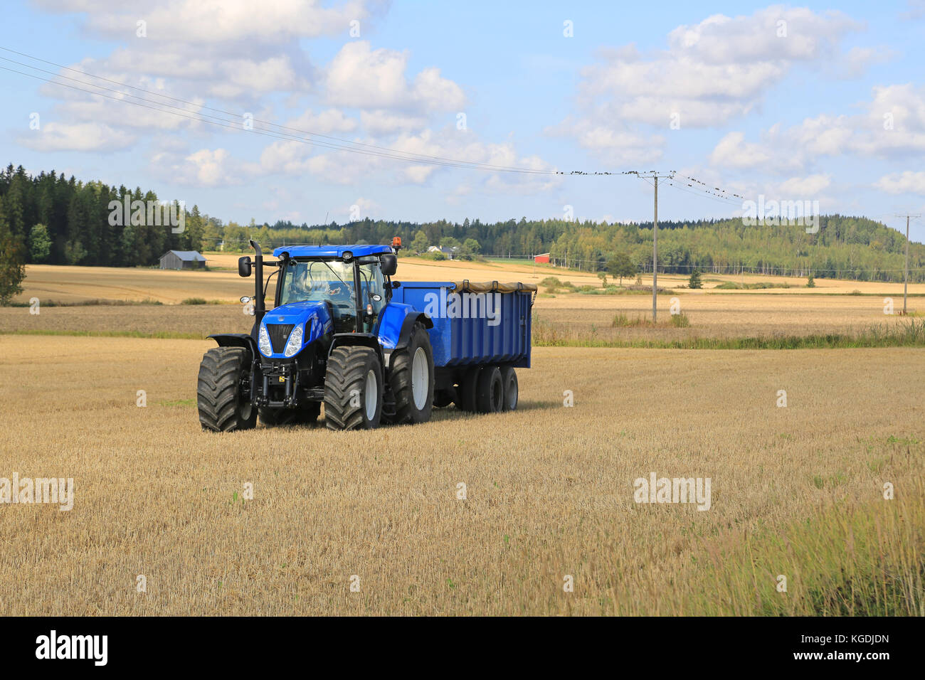 Somero, FINNLAND - 12. SEPTEMBER 2015: New Holland T 7,250 Traktor und blauer landwirtschaftlicher Anhänger auf Stoppelfeld. New Holland feiert 12 Jahrzehnte Stockfoto