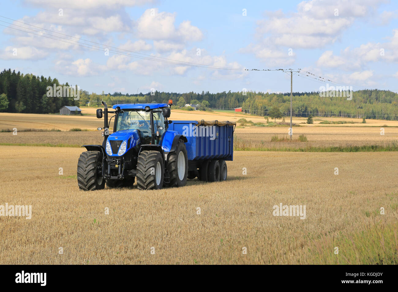 Somero, FINNLAND - 12. SEPTEMBER 2015: New Holland T 7,250 Traktor und blauer landwirtschaftlicher Anhänger auf Stoppelfeld. New Holland feiert 12 Jahrzehnte Stockfoto